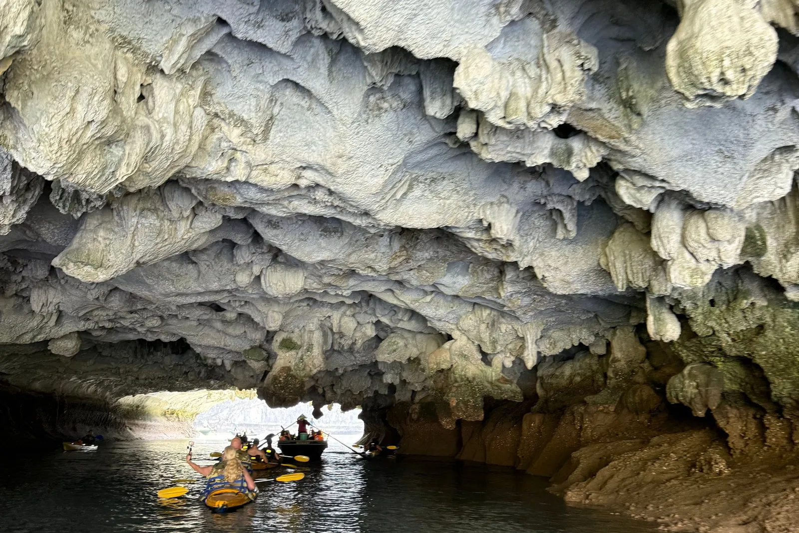 Kayaks under the mouth of a cave, the rock ceiling folding down close overhead