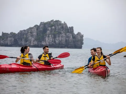 Two double kayaks side by side on flat water, four guests in life jackets paddling below a karst outcrop