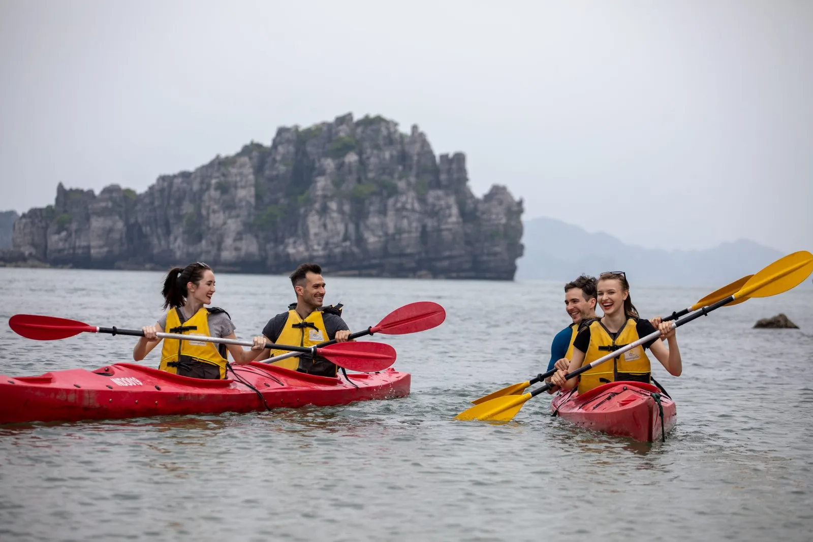 Two double kayaks side by side on flat water, four guests in life jackets paddling below a karst outcrop