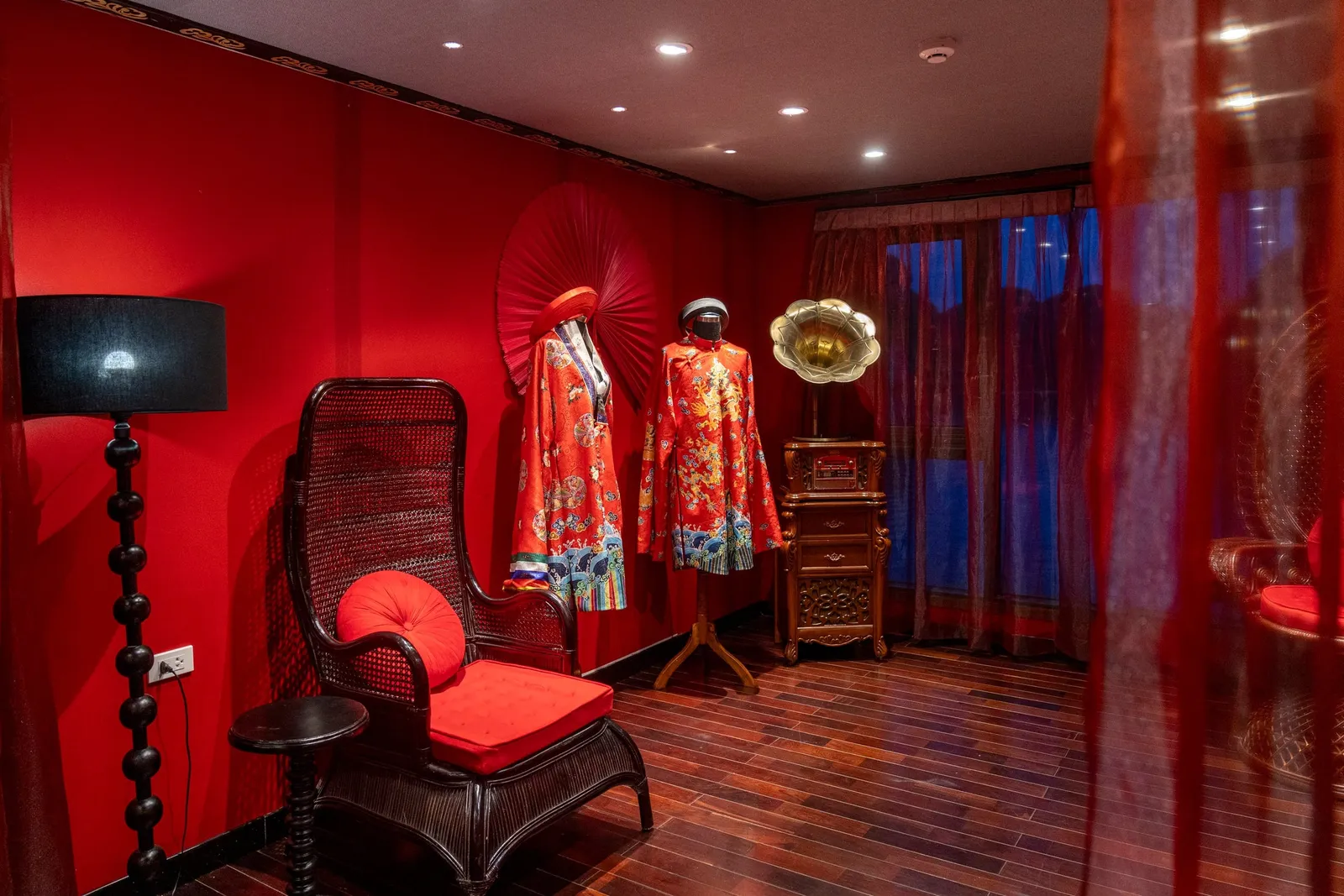 Ao dai on display in a red-walled room with a lacquer chair and a folding fan on the wall