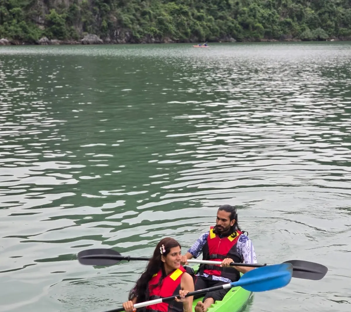 Two guests in life jackets paddling a kayak across open green water