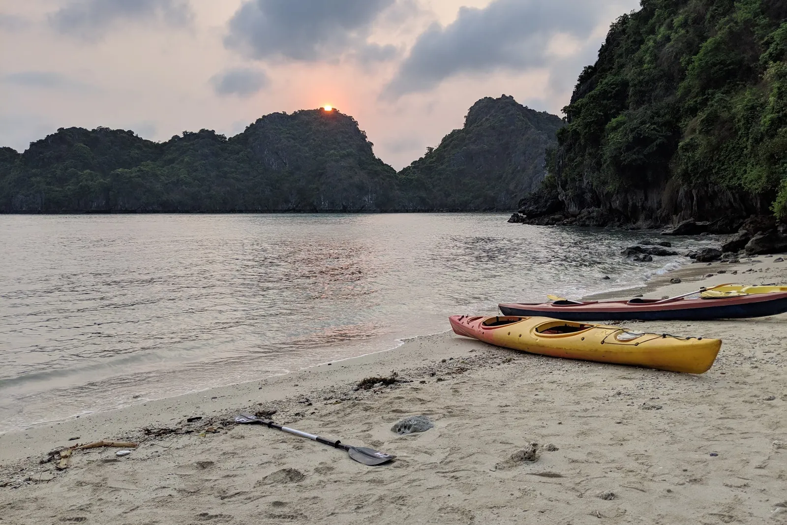 Two kayaks pulled up on a sand beach at sunset, paddles laid beside them
