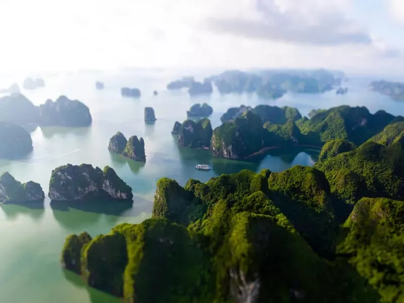 Aerial view of limestone karst islands covered in vegetation rising from calm turquoise water with a small cruise boat visible in the distance.
