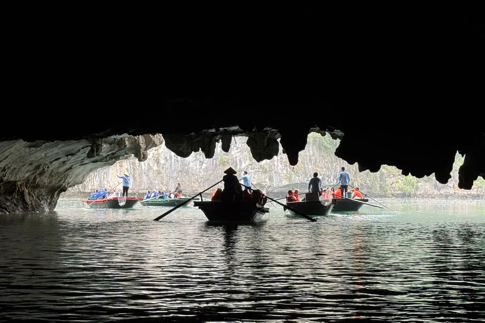 Rowing boats being paddled through a lit cave, stalactites hanging low over the water