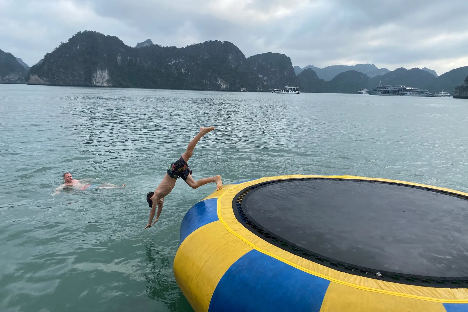 Guest diving off a floating trampoline into the bay, another swimmer already in the water