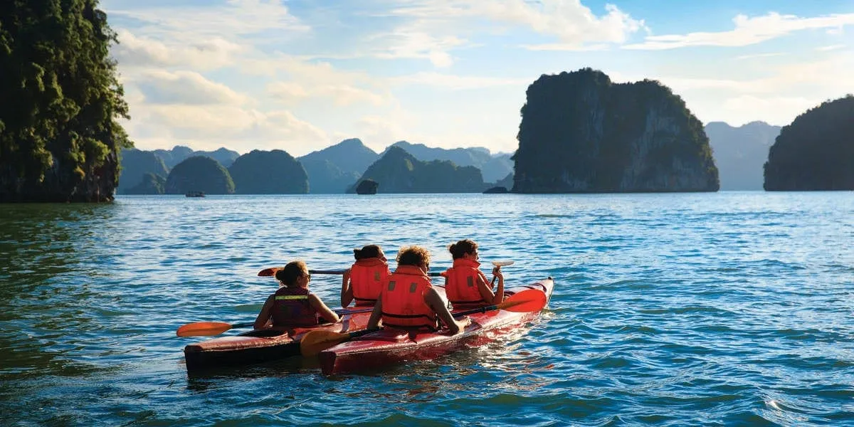Four people in red life jackets paddle a kayak on calm water with limestone karst islands in the background.