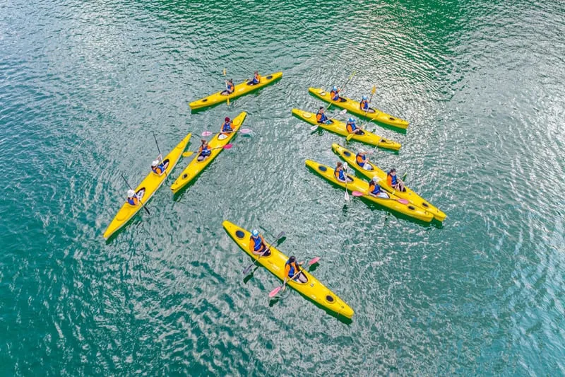 Aerial view of multiple people paddling yellow kayaks in turquoise water.