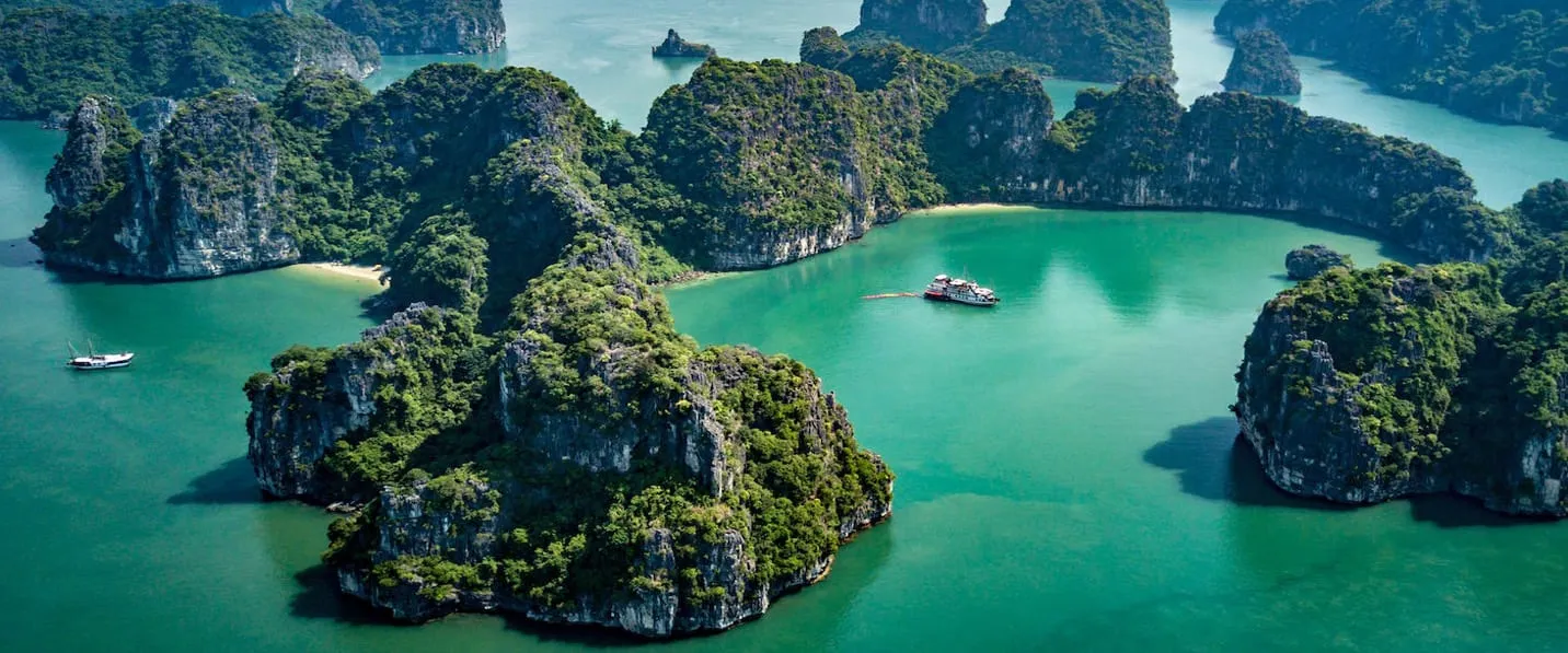 Aerial view of limestone karst islands surrounding turquoise water with two small boats visible in the bay.