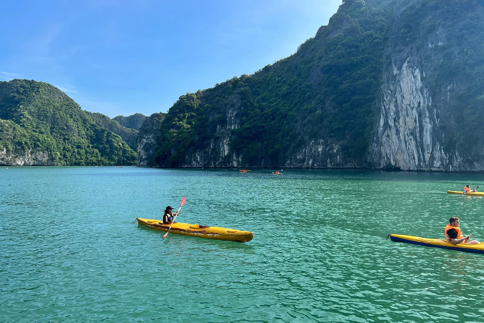 Two kayaks on flat green water at the foot of a sheer limestone cliff