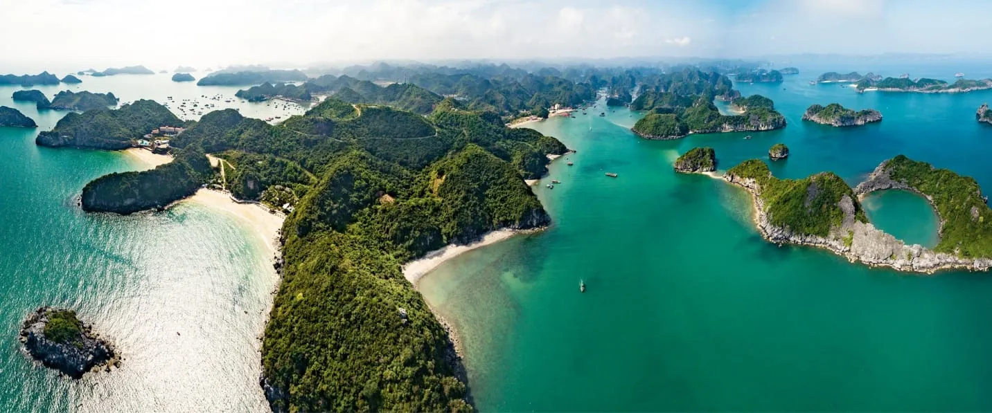 An aerial view of emerald water with forested limestone karst islands and white sand beaches.