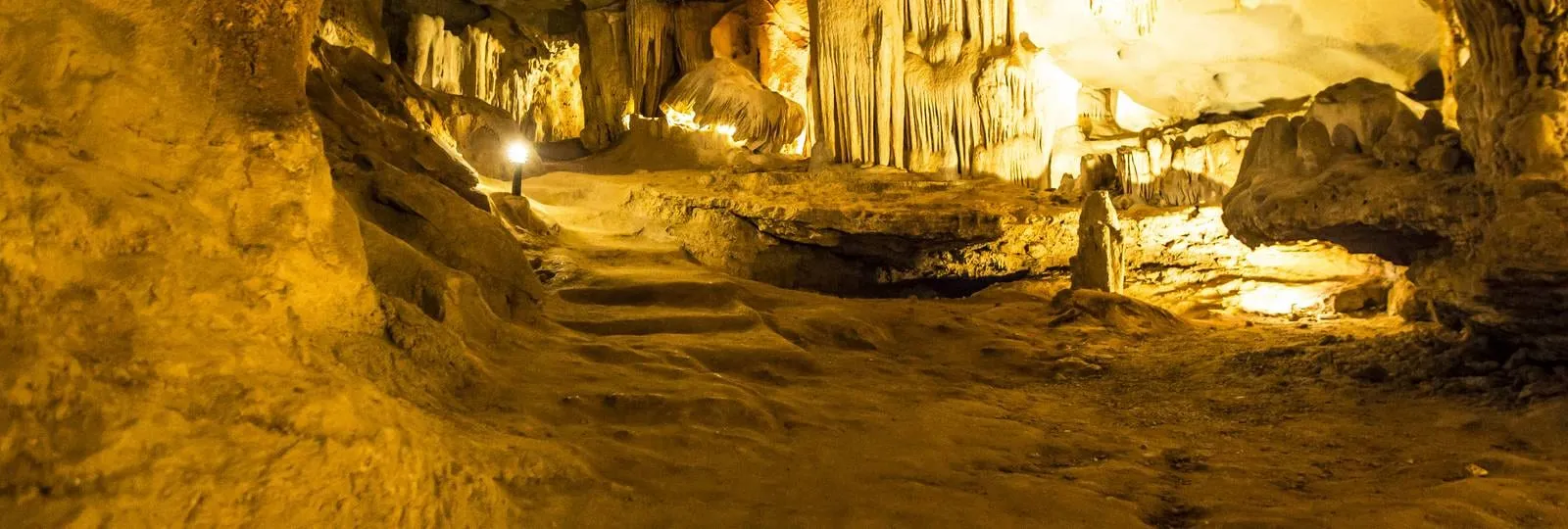 Inside Thien Canh Son cave, lit stalactites running down to a sand floor with a walkway cut through
