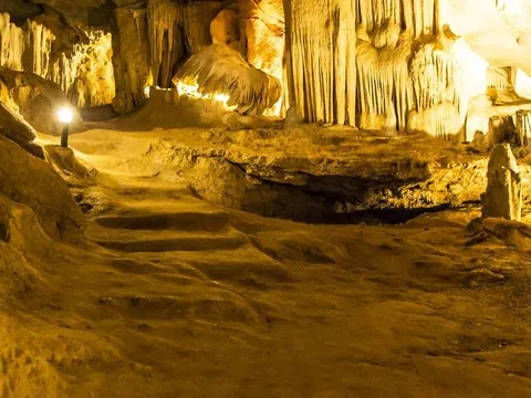Inside Thien Canh Son cave, lit stalactites running down to a sand floor with a walkway cut through