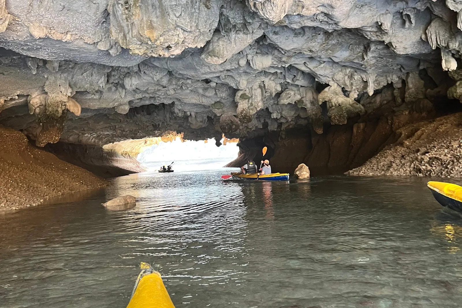 Paddling out through a cave mouth, daylight and moored kayaks framed in the opening ahead