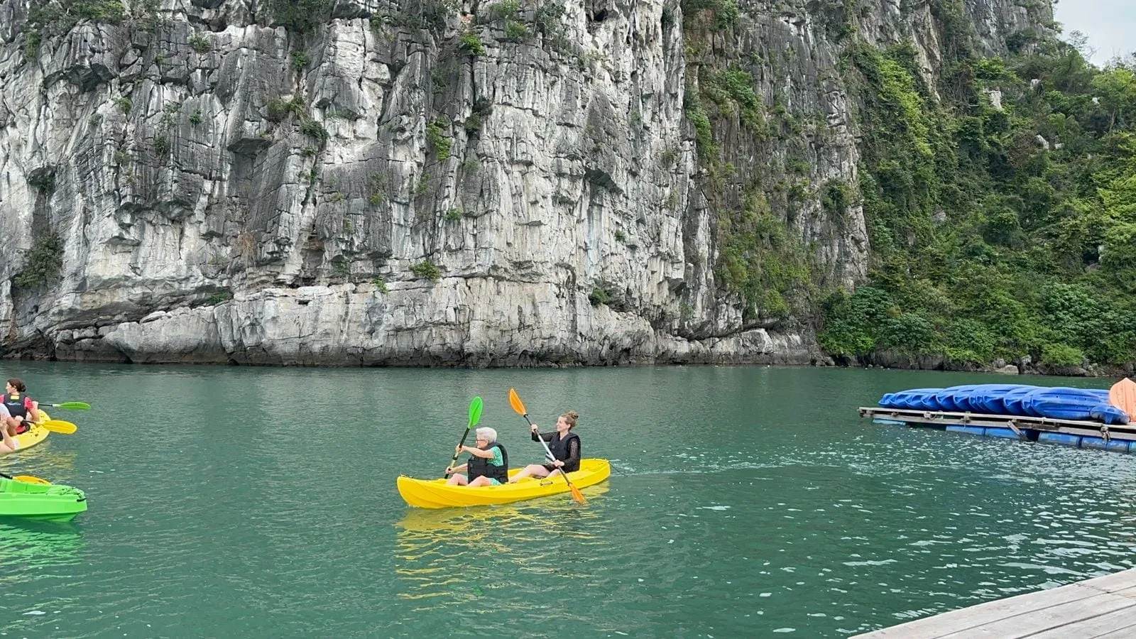 A pair of guests paddling a yellow kayak along the foot of a limestone cliff