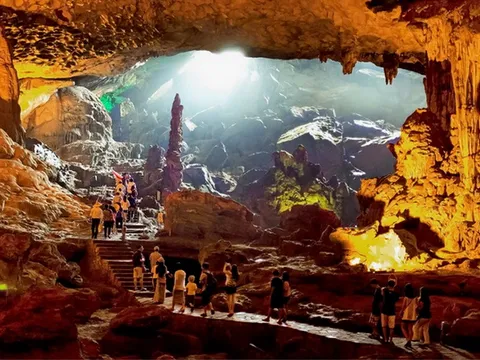 Tourists walk through a large illuminated cave with stalactites and stalagmites, with wooden stairs and platforms throughout.