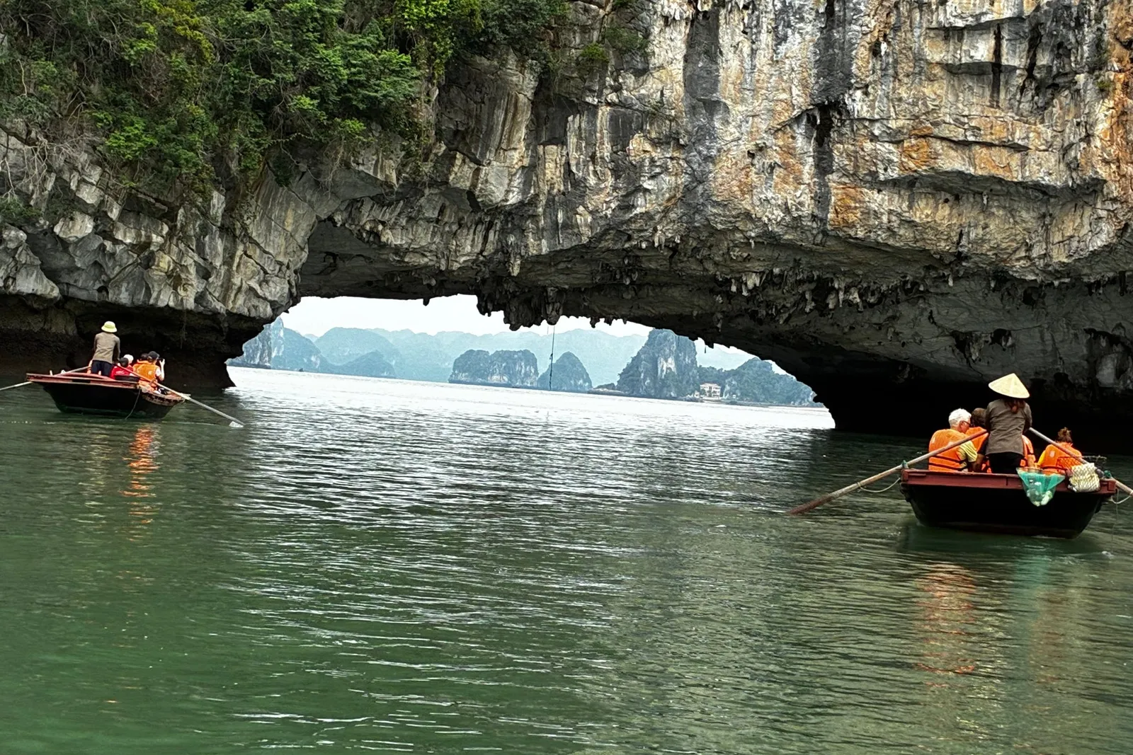 Rowing boats passing under a natural rock arch, the bay opening out on the far side