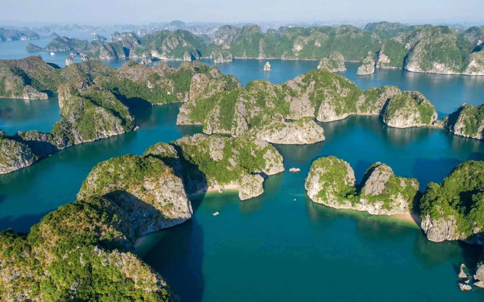 Aerial view of limestone karst islands rising from turquoise water with small boats visible between the formations.