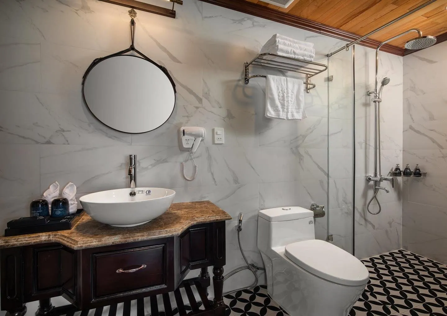 Bathroom in white marble with a round mirror, a stone basin on a dark timber vanity and a walk-in shower