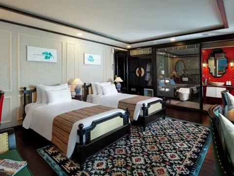 A luxury cabin interior with two beds, decorative rug, and glass-walled bathroom with red accent wall.