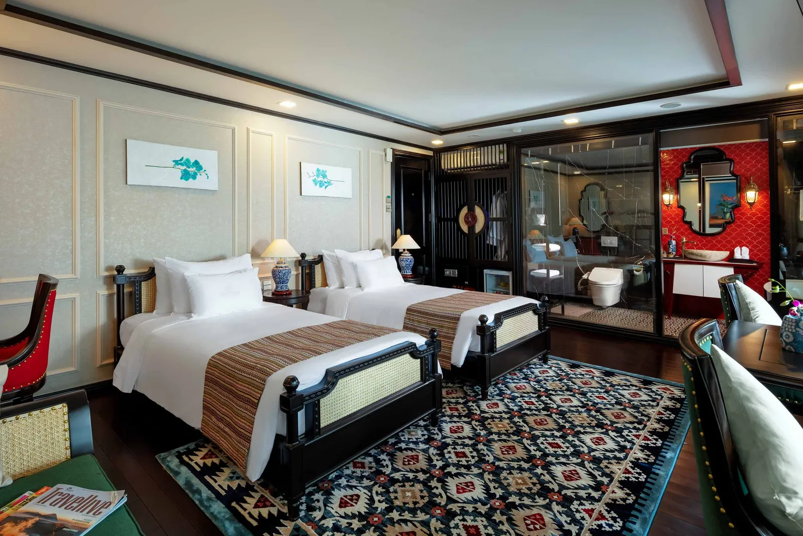 A luxury cabin interior with two beds, decorative rug, and glass-walled bathroom with red accent wall.