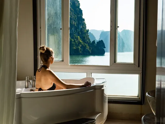 A person in a bathtub inside a cabin with windows showing limestone karst islands and calm water outside.