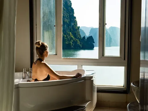 Guest in a freestanding bath looking out through the cabin window at karst cliffs across the water