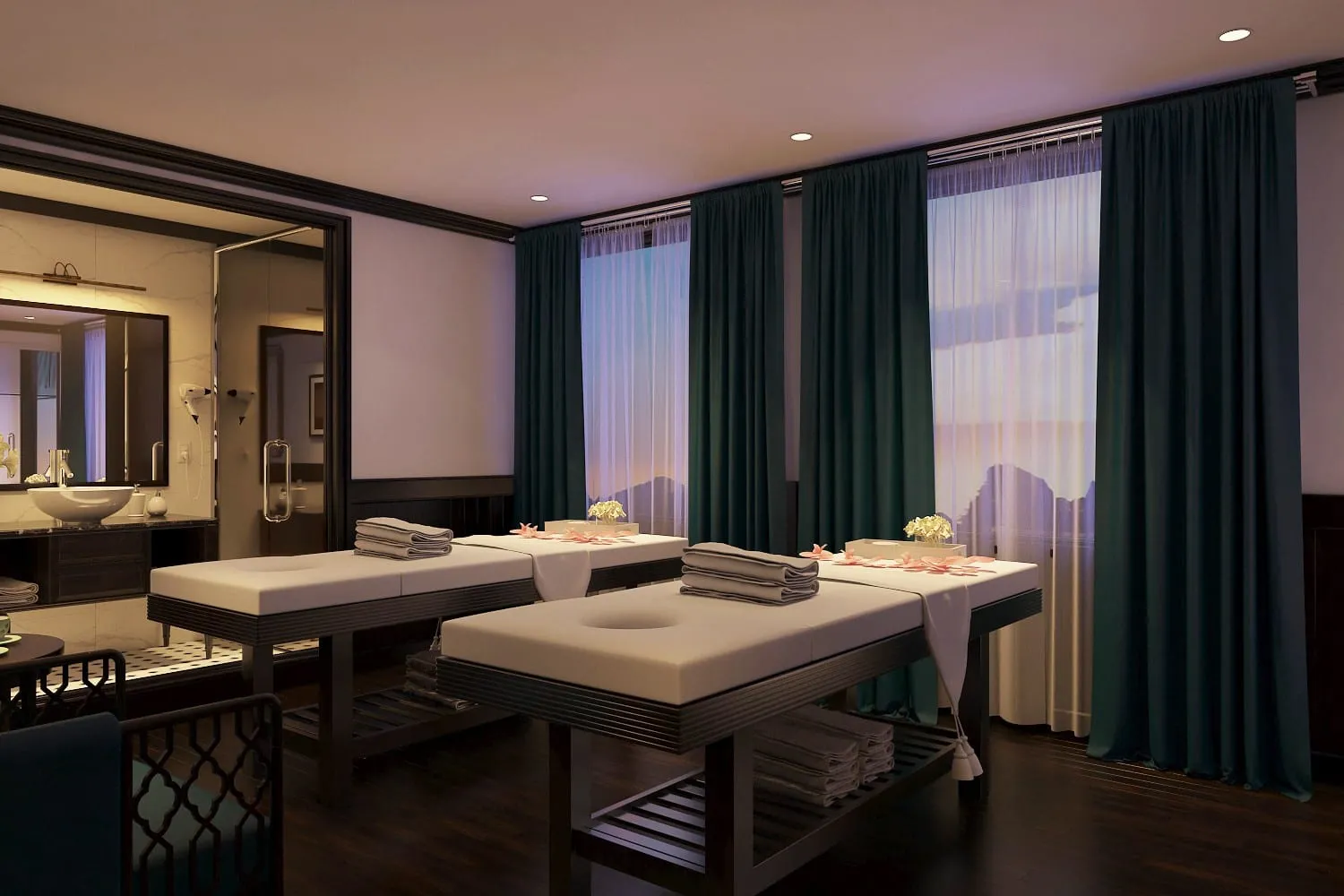 A spa or massage treatment room with two massage beds, dark green curtains covering large windows, and an ensuite bathroom visible on the left.