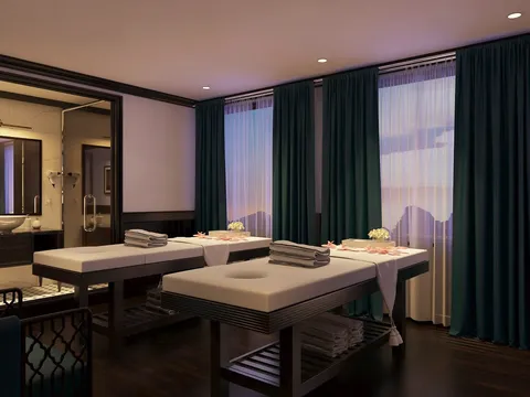 A spa or massage treatment room with two massage beds, dark green curtains covering large windows, and an ensuite bathroom visible on the left.