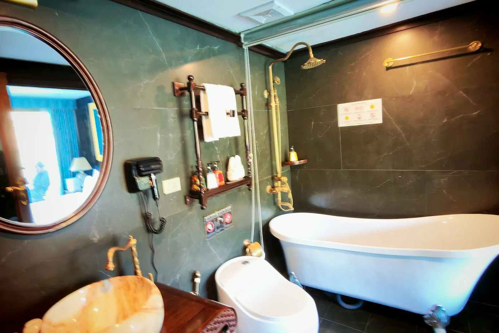 Bathroom in green marble with a freestanding tub, brass fittings and a round mirror above the basin
