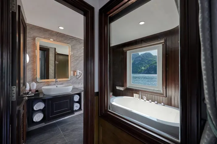 A luxury boat cabin bathroom with a bathtub positioned beside a window showing a limestone karst island and water.