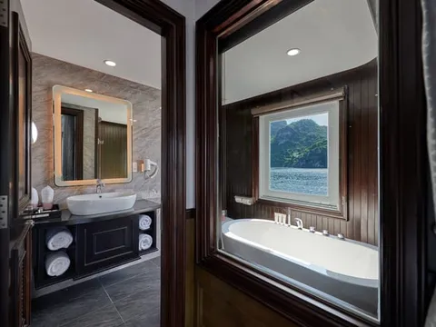 A luxury boat cabin bathroom with a bathtub positioned beside a window showing a limestone karst island and water.