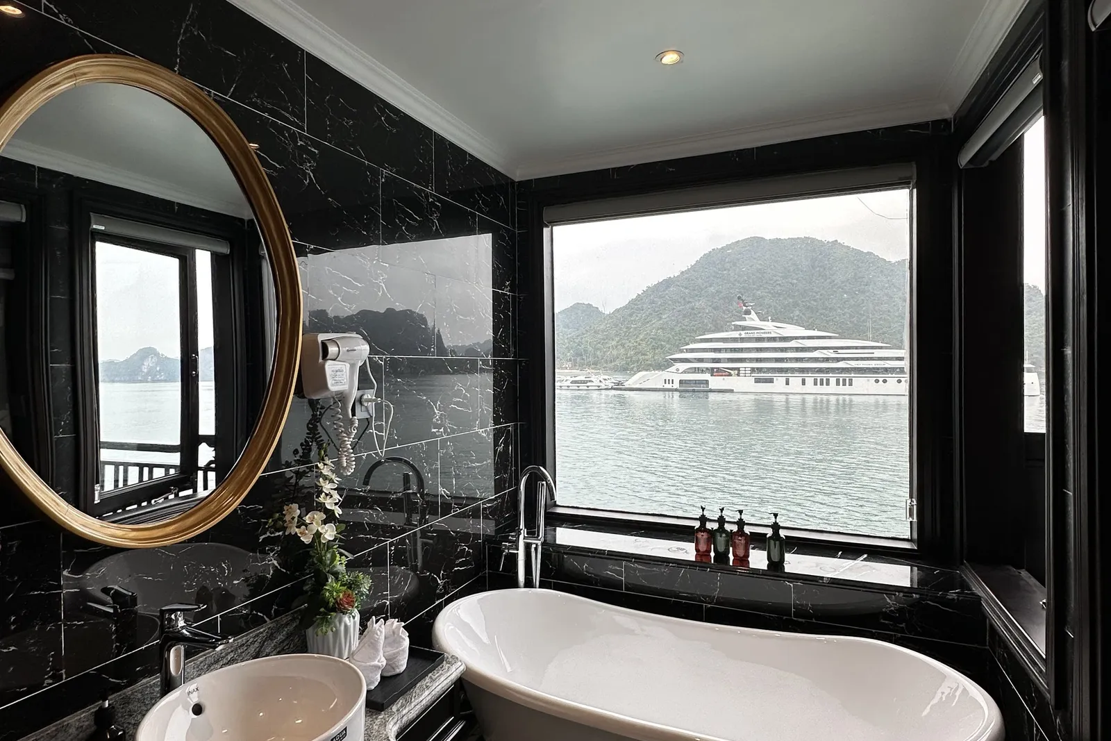 Bathroom in black marble with a freestanding tub set against the window, an oval mirror above the basin