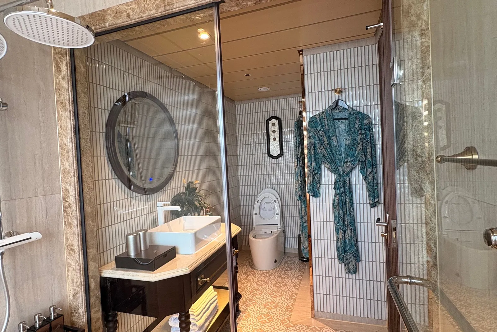 Bathroom in pale marble with a walk-in shower, twin robes hanging and a round mirror over the basin