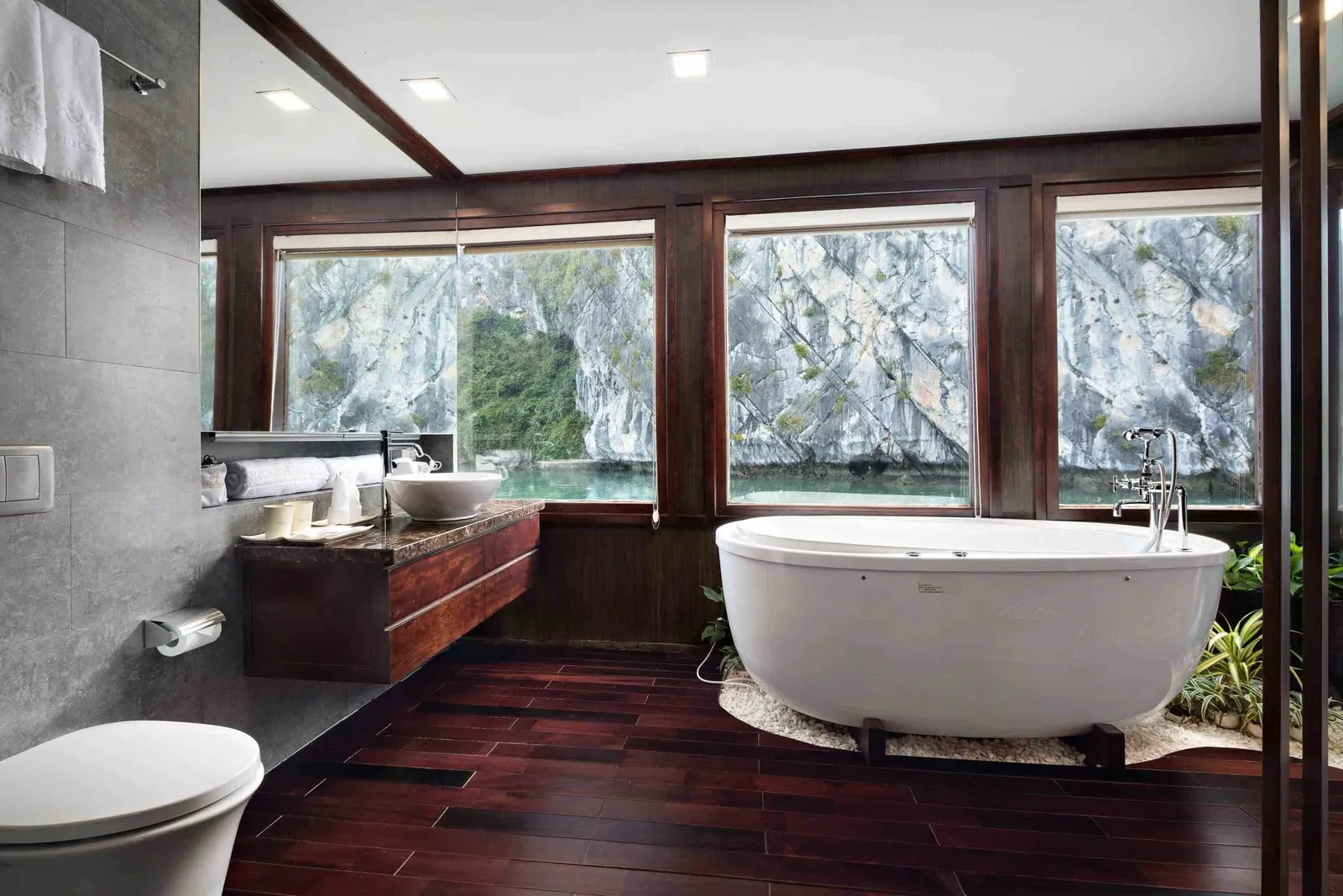 A luxury bathroom with freestanding tub and dark wood floors overlooking limestone karst formations through large windows.