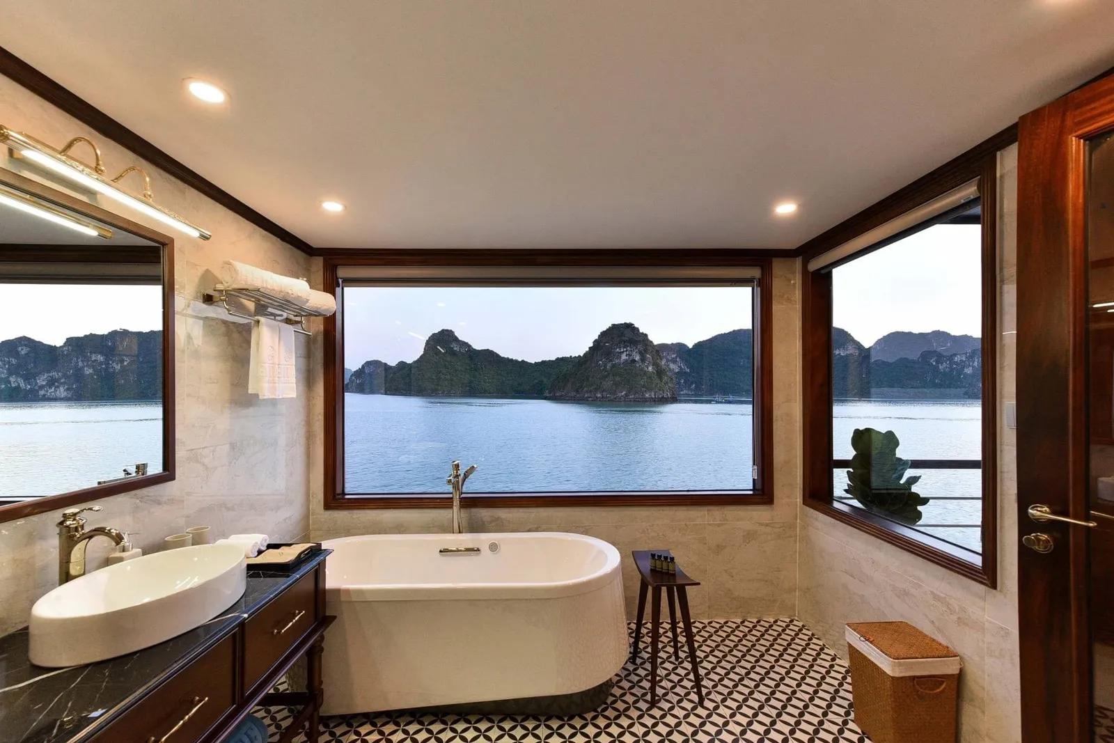 A cabin bathroom with a freestanding tub, vessel sink and mirror, with large windows looking out on calm water and limestone karst islands.
