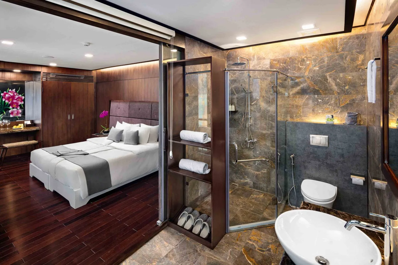 A luxury cabin interior with a bed, glass-enclosed shower, and marble bathroom fixtures.
