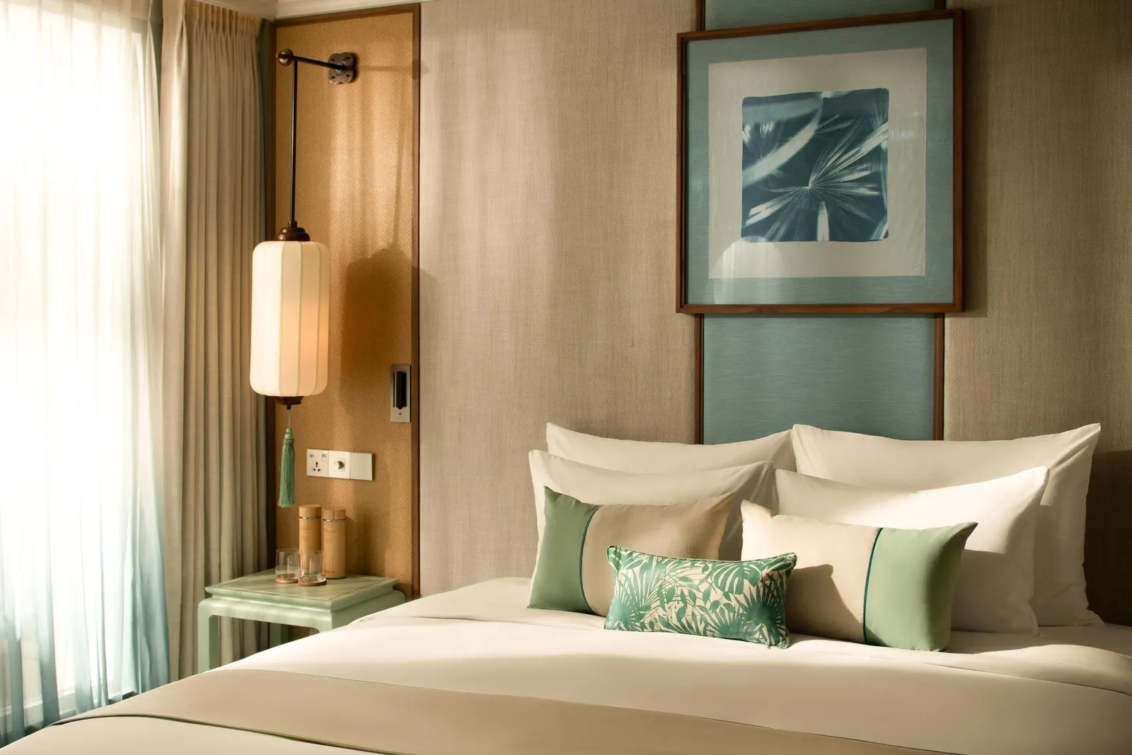 A hotel-style cabin interior with a bed, decorative pillows, wall art, bedside lamp, and curtained window.