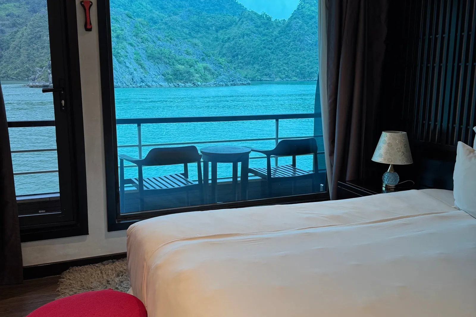 Cabin opening onto a private balcony with two chairs, turquoise water and a green cliff right outside