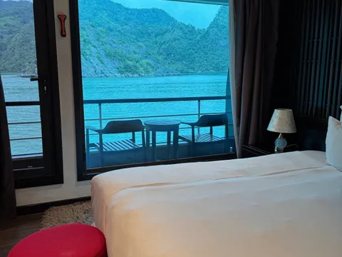 Cabin opening onto a private balcony with two chairs, turquoise water and a green cliff right outside