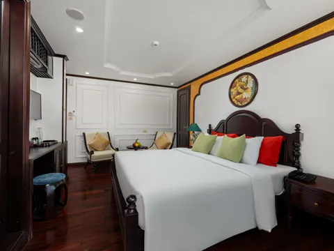 An interior cabin with a bed, dark wood furniture, white walls with yellow trim, and two chairs near a window.