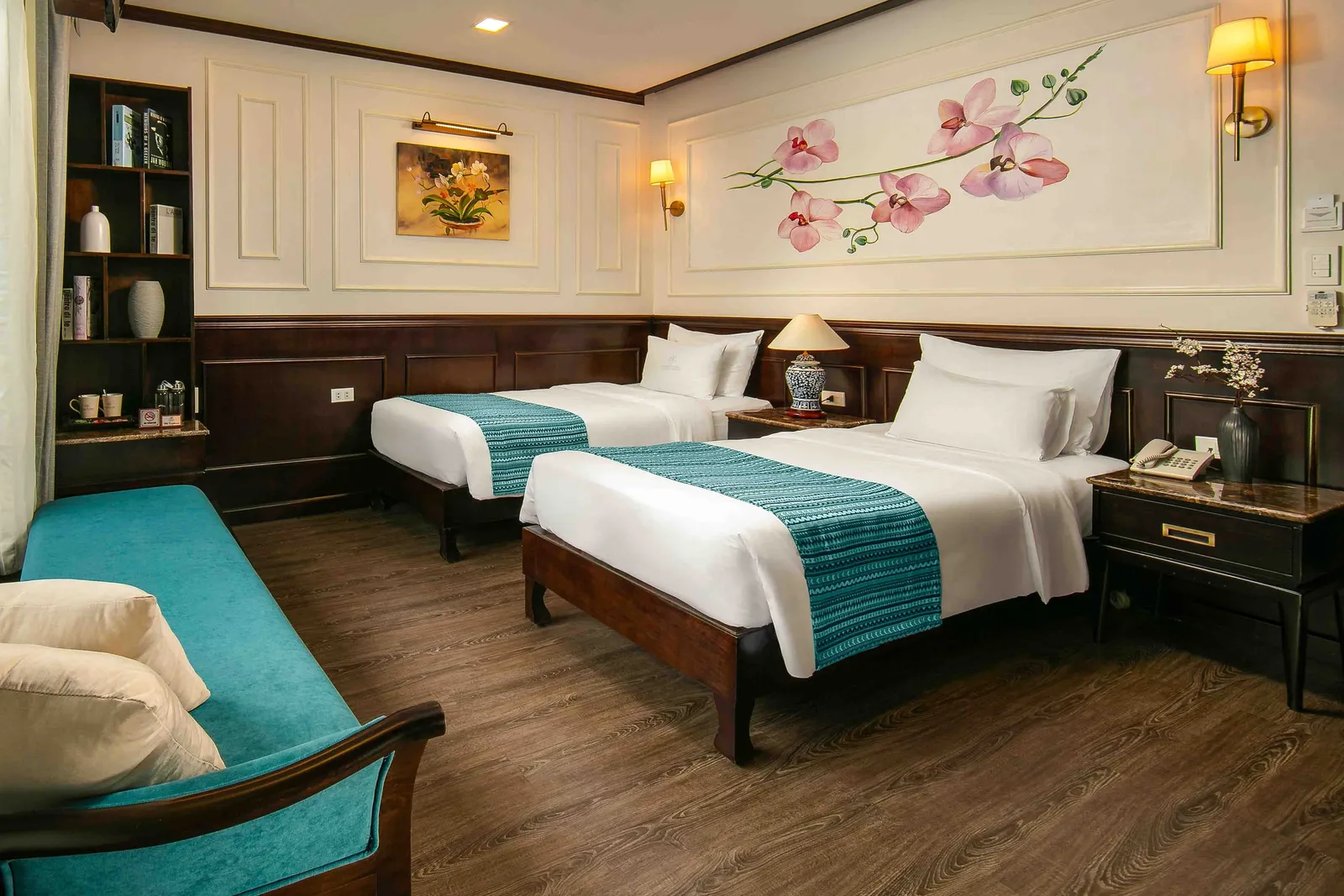 A cruise ship cabin with two twin beds, dark wood furniture, white paneled walls with orchid artwork, teal accents, and warm lighting.