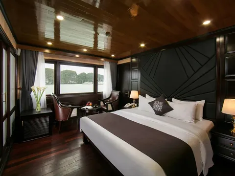 A luxury boat cabin with dark wood paneling, white bedding, and a window view of karst limestone formations on water.