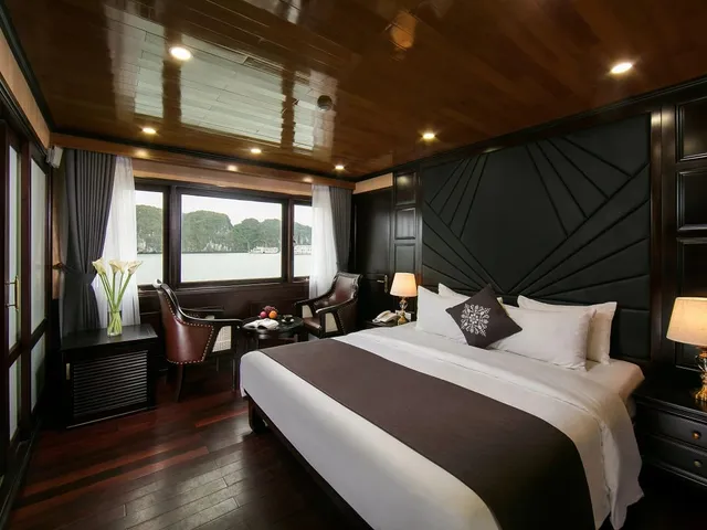A luxury boat cabin with dark wood paneling, white bedding, and a window view of karst limestone formations on water.