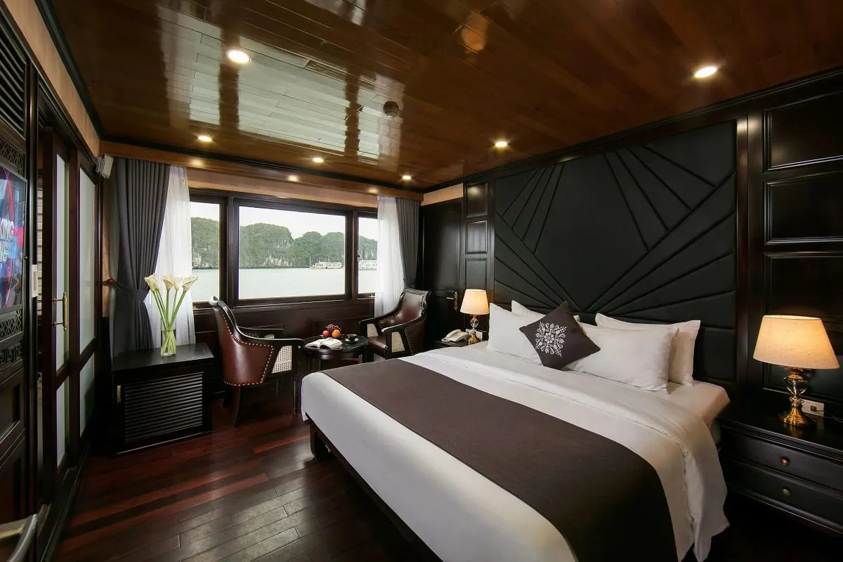A luxury boat cabin with dark wood paneling, white bedding, and a window view of karst limestone formations on water.