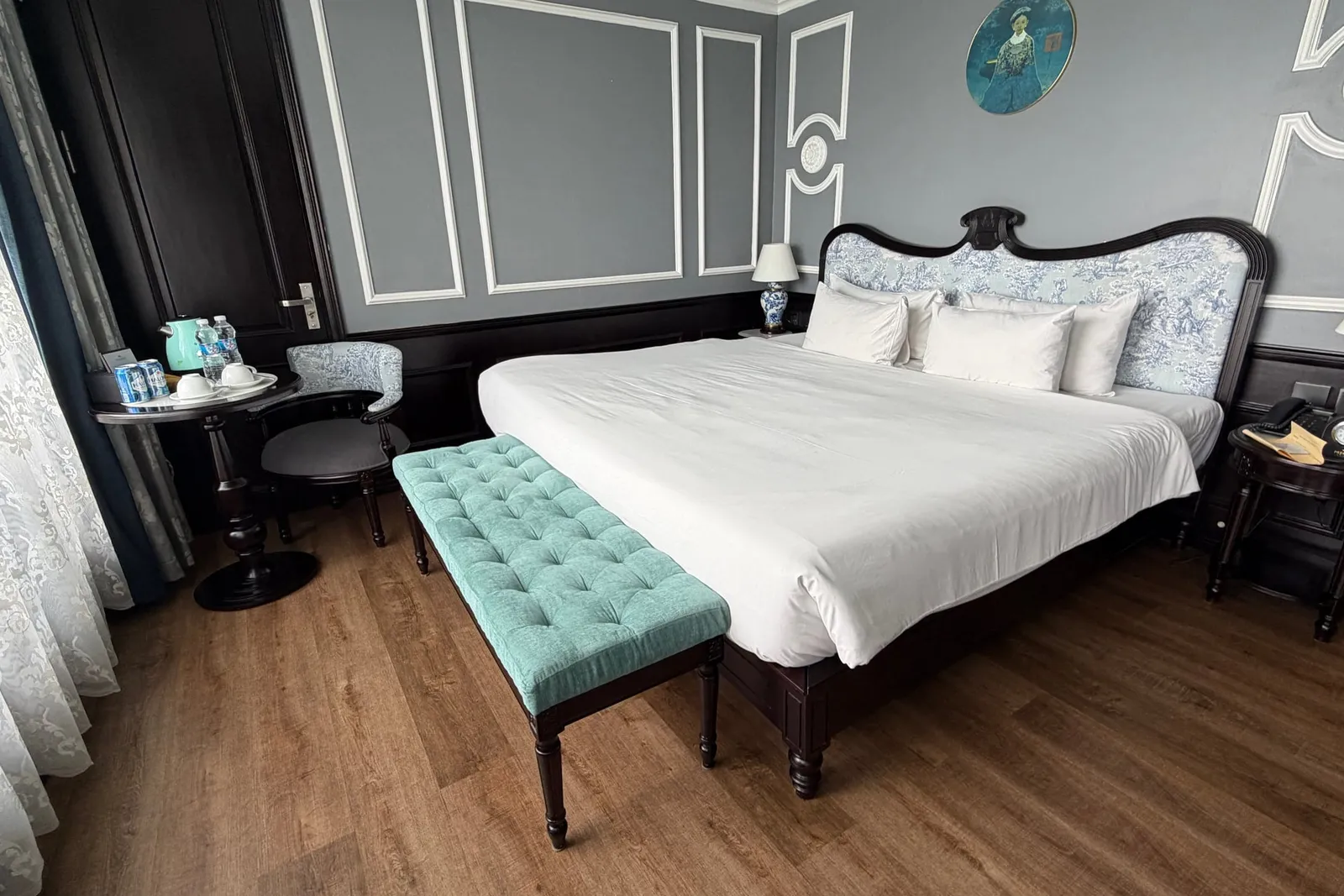 Cabin in grey panelling with a carved bedhead and a buttoned teal bench at the foot of the bed