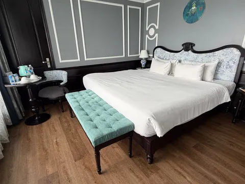 Cabin in grey panelling with a carved bedhead and a buttoned teal bench at the foot of the bed