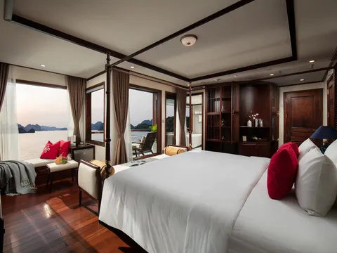 A luxury cabin interior with a white bed, dark wood furnishings, and large windows showing limestone karst islands on calm water.