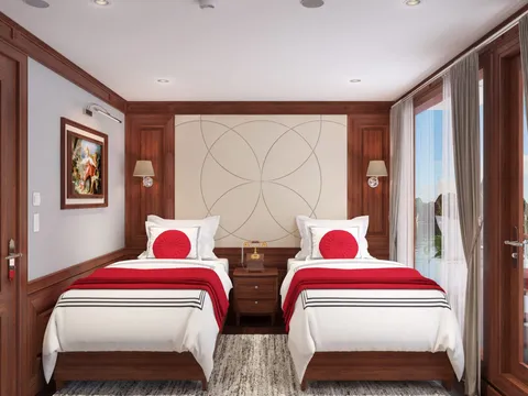 A cabin interior with two twin beds, dark wood paneling, white and red bedding, and windows showing daylight outside.