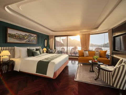 A luxury cabin interior with a bed, orange sofa, and large windows showing karst mountains and water at sunset.
