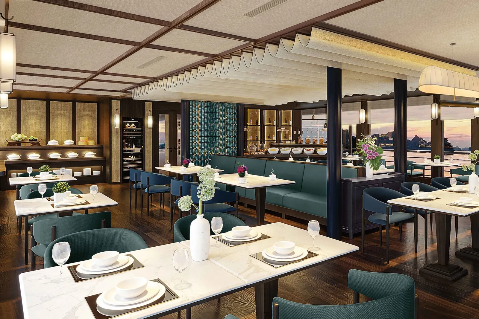 An upscale dining room interior with dark wood floors, teal upholstered seating, white-topped tables set with plates and glasses, and large windows showing karst limestone formations and water at sunset.